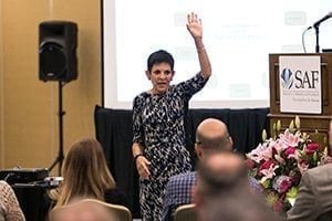 Glenna Hecht with her left hand raised in the air. She was speaking at an SAF event in 2015