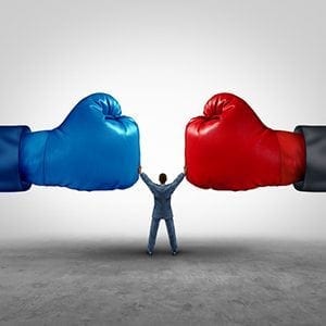 stock image of two boxing gloves with a man in the middle holding up. The boxing gloves are Red and blue.