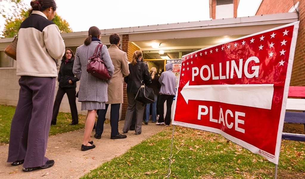 Voting polling place sign and people lined up on election day.